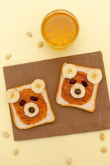 Fototapeta na wymiar Funny cute bear faces sandwich toast bread with peanut butter, banana,nuts,juice. Kids childrens baby's sweet dessert healthy breakfast lunch food art on plate,close up,top view