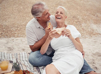 Love and healthy senior couple on picnic at a beach eating sandwich with funny conversation for...