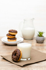 Mini donuts covered with chocolate glaze served with bottle, jug, glass of milk. Stack of tasty sweet sugar creamy or icing doughnuts dessert food on plate and napkin on kitchen. national donuts day