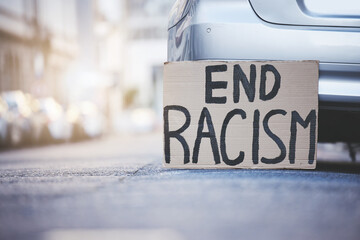 End racism sign cardboard poster in urban street background for solidarity, human rights and race...