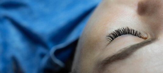 Eye lash extension procedure. Young beautiful woman eye with long false eyelashes. Close up macro...