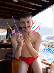Handsome young man wearing speedo dancing. Holding colorful drinking straws on his hand. Straws are like Wolverine's claws. Enjoy, fun, holiday and summer concept.