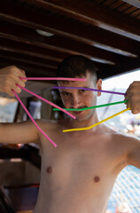 Fototapeta na wymiar Handsome young man wearing speedo dancing. Holding colorful drinking straws on his hand. Straws are like Wolverine's claws. Enjoy, fun, holiday and summer concept.