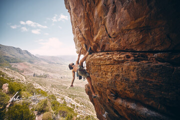 Rock climbing, rope and fearless mountain climber on a cliff, big rocks and risky challenge alone in summer. Mountaineering, bouldering and strong man training his body for balance outdoors in nature - obrazy, fototapety, plakaty