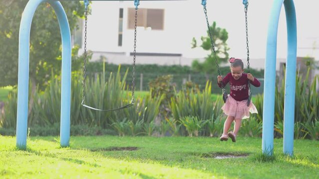 Ni&ntilde;a hermosa y feliz latina rubia colgada en un columpio divertida y disfrutando en el parque en un charco de agua y tierra y lodo al aire libre al exterior en un hermoso d&iacute;a