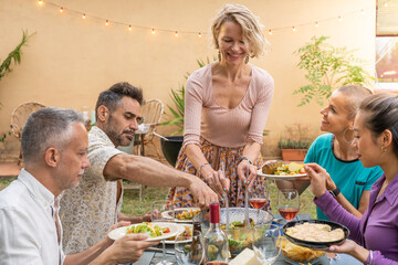 Multiethnic mature friends eating enjoying happy smiling and laughing in the backyard at home togetherness concept.