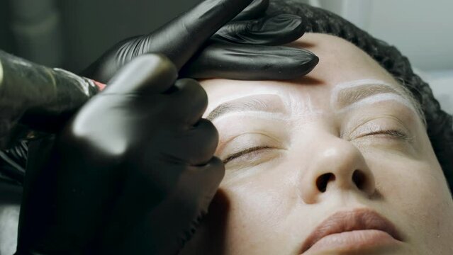 A special needle tattoo machine makes a permanent make-up correction of a woman's eyebrows. Microblading, powder coating close-up.