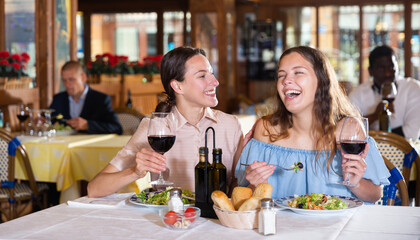 Two girls are discussing something fun at a table in a restaurant