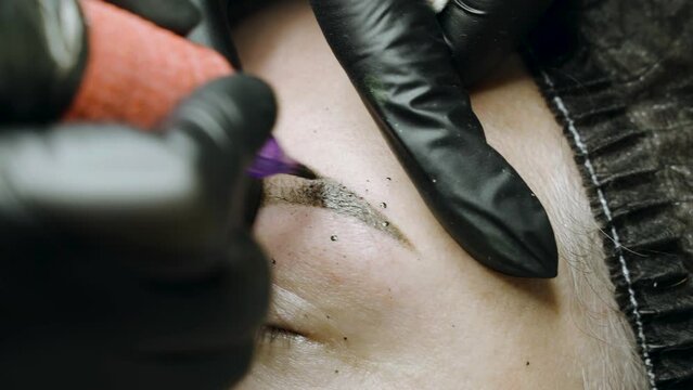 A special needle tattoo machine makes a permanent make-up correction of a woman's eyebrows. Microblading, powder coating close-up.