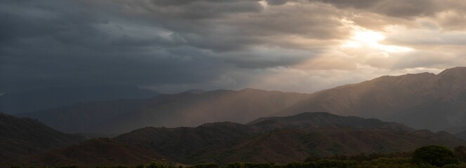 Panorama of hills with sunrays galling on the peak and clouds covering the sky at sunrise