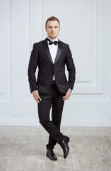 Attractive young man standing in tuxedo and looking at camera
