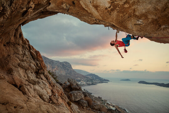 Male rock climber climbing along a roof in cave at sunset