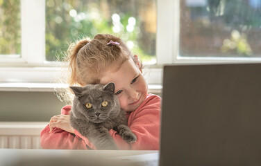 girl kid child in front of a laptop cuddling holding a cat 