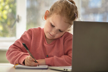 kid child studying writing in a notebook next to computer laptop 