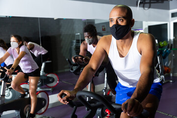 Obraz na płótnie Canvas Men and women wearing protective masks ride stationary bike in a fitness club