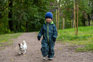 a two-year-old toddler boy walks in the forest in autumn with his dog Jack Russell Terrier