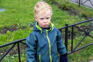 A two-year-old kid stands at the fence and pouted offendedly. Looks into the camera. Portrait....