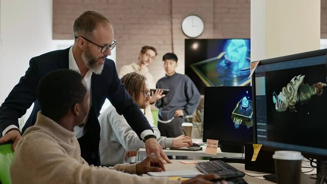 The CEO of the company studio developers of games and applications discusses with the artist a 3D model on a computer against the background of other employees of the company.