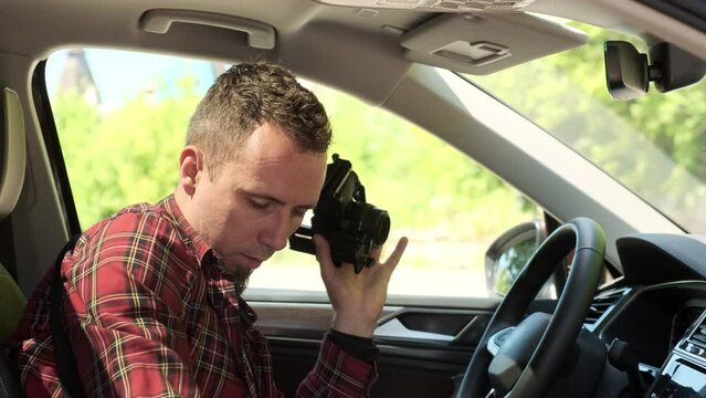 professional photographer sits in car and prepares car for shooting, cleans it. man in plaid shirt with camera in his hand sitting in small SUV.