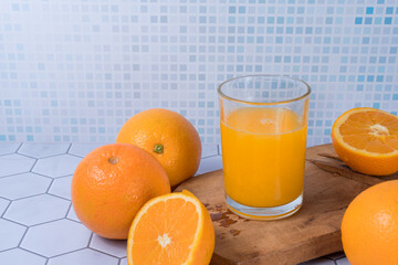 Glass of orange juice squeezed over a board and oranges around it.