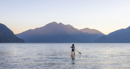 Adventurous Woman Paddling on a Paddle Board in a peaceful lake.