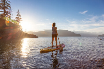Adventurous Woman Paddling on a Paddle Board in a peaceful lake.