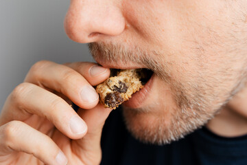 Close-up of middle-aged man with beard taking bite off healthy oatmeal raisin cookie, traditional and popular biscuit in America made of sugar, flour, rolled oats, eggs and dried raisins - 531551118