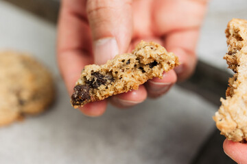 Close up of male hand breaking freshly baked oatmeal raisin cookie in half, healthy, traditional and popular American biscuit recipe made of flour, sugar, eggs, rolled oats, dried fruit, baking soda - 531551119
