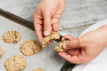 Close up of male hand breaking freshly baked oatmeal raisin cookie in half, healthy, traditional and popular American biscuit recipe made of flour, sugar, eggs, rolled oats, dried fruit, baking soda - 531551125