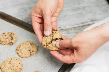 Close up of male hand breaking freshly baked oatmeal raisin cookie in half, healthy, traditional and popular American biscuit recipe made of flour, sugar, eggs, rolled oats, dried fruit, baking soda - 531551129