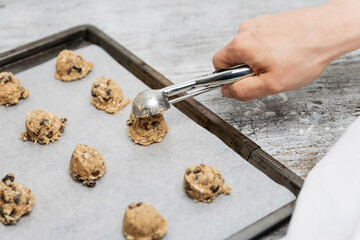 Hand of male baker scooping raw oatmeal raisin cookie dough with scoop on cookie sheet with baking...