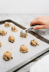 Hand of male baker scooping raw oatmeal raisin cookie dough with scoop on cookie sheet with baking paper, traditional and most popular American biscuit recipe made of flour, sugar, eggs, rolled oats - 531551137