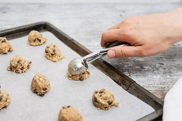 Hand of male baker scooping raw oatmeal raisin cookie dough with scoop on cookie sheet with baking paper, traditional and most popular American biscuit recipe made of flour, sugar, eggs, rolled oats - 531551141