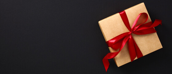 Black Friday sale banner design. Craft paper gift box wrapped red ribbon bow on black background.