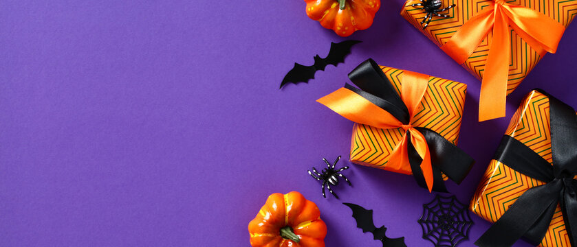 Happy Halloween banner. Festive background with gift boxes, orange pumpkins, bats, spiders on purple table. Halloween header, wide banner design.