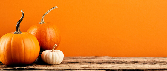 Fototapeta Three decorative pumpkins on wooden tabletop on orange background. Autumn holidays banner design. Thanksgiving, Harvest concept. obraz