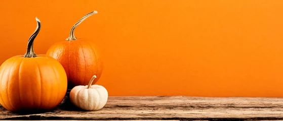 Foto op Plexiglas Three decorative pumpkins on wooden tabletop on orange background. Autumn holidays banner design. Thanksgiving, Harvest concept. © photoguns