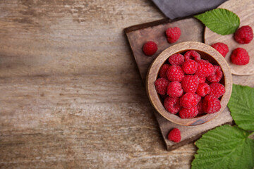 Bowl with fresh ripe raspberries and green leaves on wooden table, flat lay. Space for text