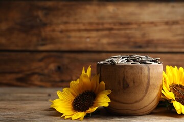 Obraz na płótnie Canvas Raw sunflower seeds and flowers on wooden table. Space for text