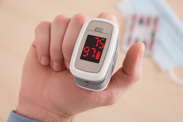 Man measuring oxygen level with modern fingertip pulse oximeter on blurred background, closeup
