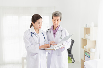 Asian doctor talking with health worker about patient treatment order, she holding patient chart and write medical list on doctor note