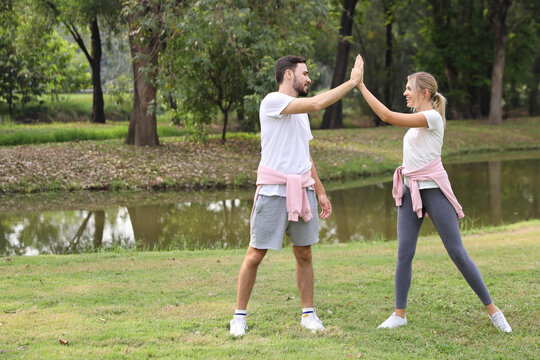 image of young caucasian couple man and woman enjoying in exercising and give me five outdoor with smiling faces and eyes contact together with green trees during summer time in the park