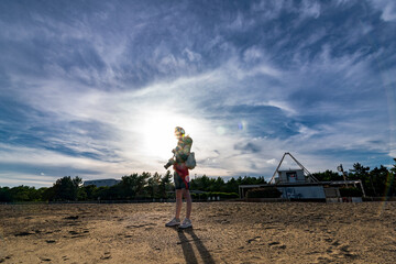 Fototapeta na wymiar 浜辺で太陽を背に、カメラを持って立っている少女