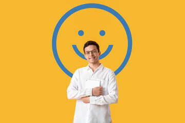 Handsome young man with tablet computer and drawn smile on yellow background