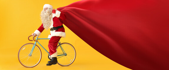 Santa Claus with big bag riding bicycle on yellow background. Banner for design