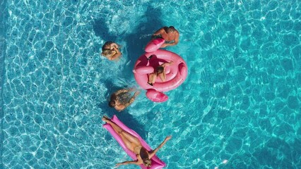 Overhead drone shot of multi-generation family with baby boy on summer holiday relaxing on inflatables and splashing in swimming pool - shot in slow motion