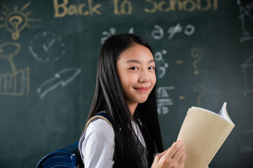 Back to school. Portrait of smiling woman child student of black chalk board, Happy beautiful Asian Schoolgirl girl standing holding books standing in front blackboard of classroom, Education lesson