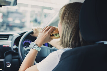 woman eating burger while driving car in the city.