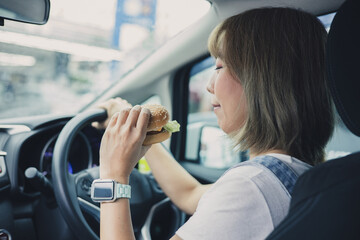 woman eating burger while driving car in the city.