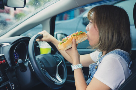 Young And Cheerful Woman Eating Healthy Sandwich With Salad Homemade While Driving Car In The City.